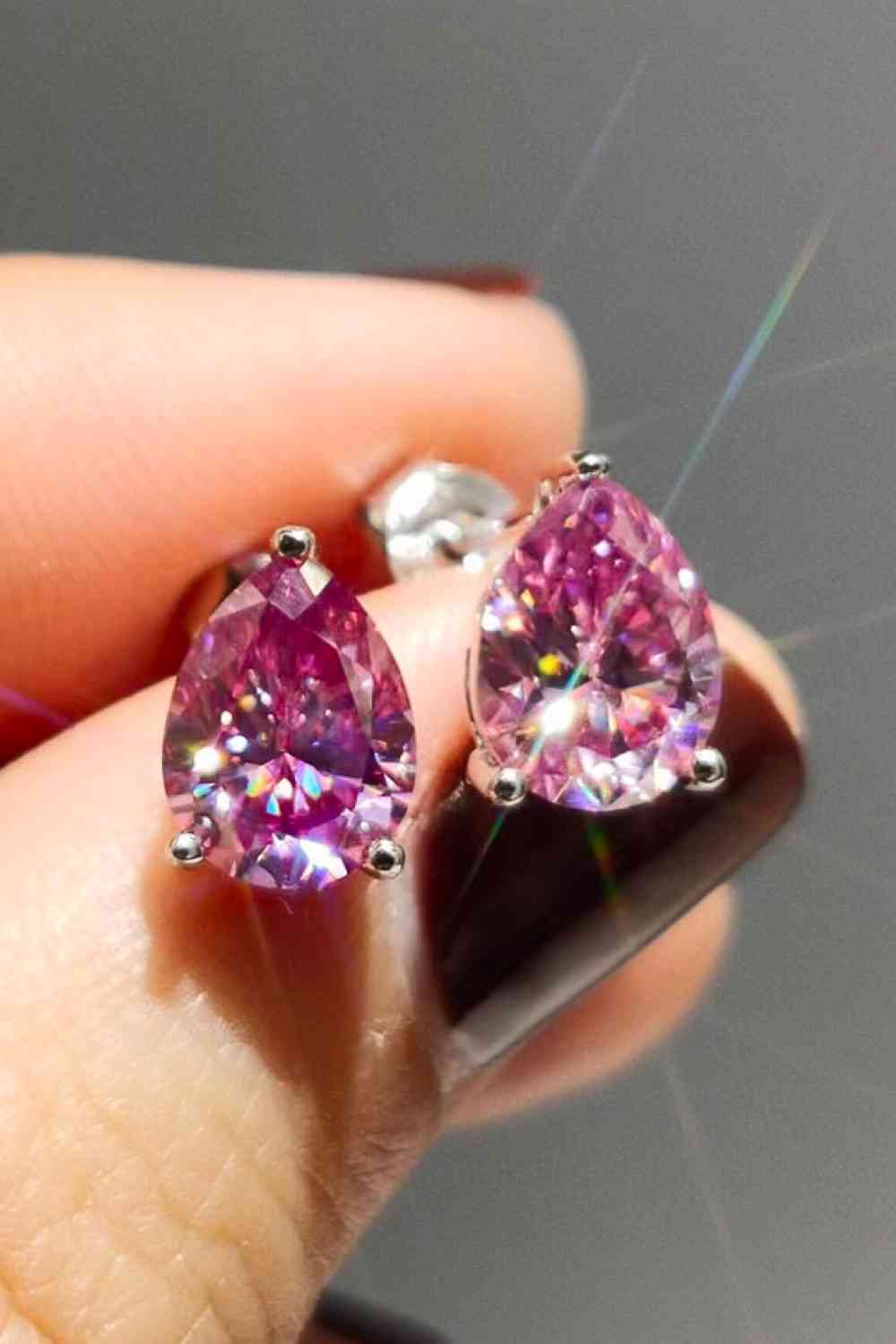 a person holding a pair of pink diamond earrings