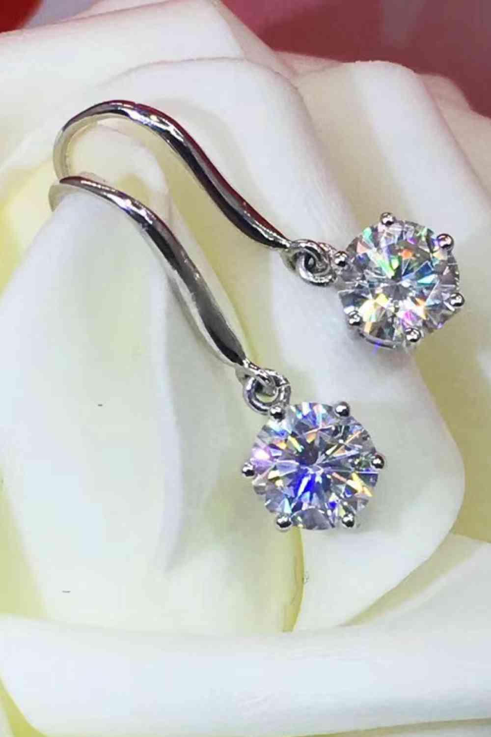 a pair of diamond earrings sitting on top of a white rose