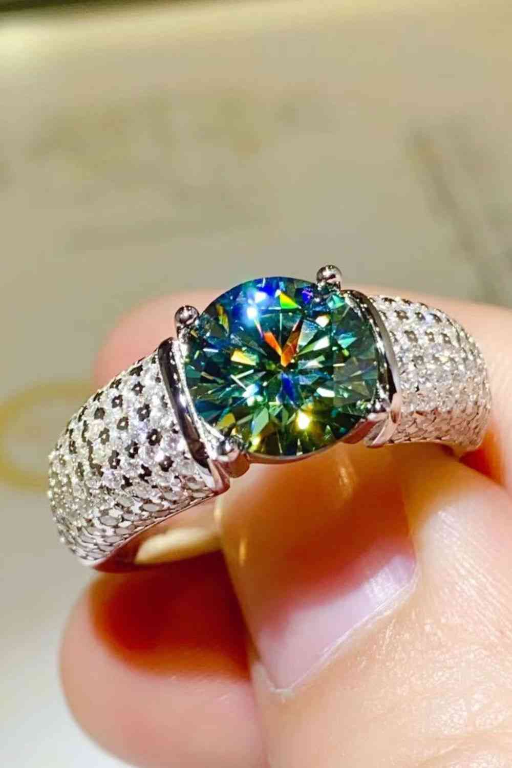 a person holding a ring with a blue and green diamond