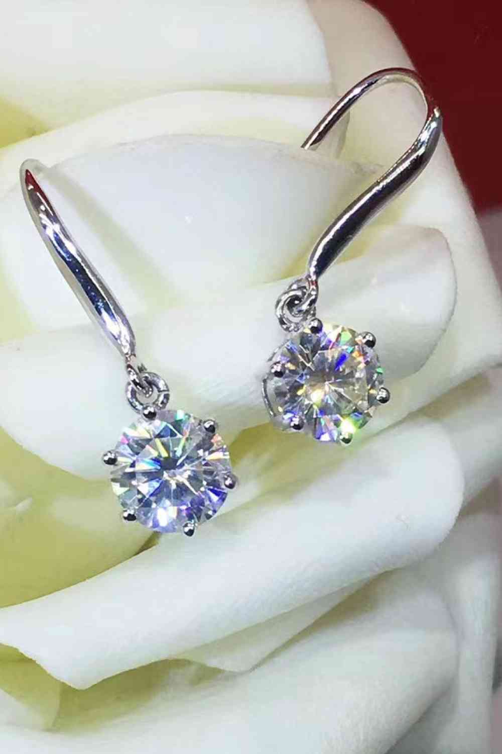 a pair of diamond earrings sitting on top of a white rose
