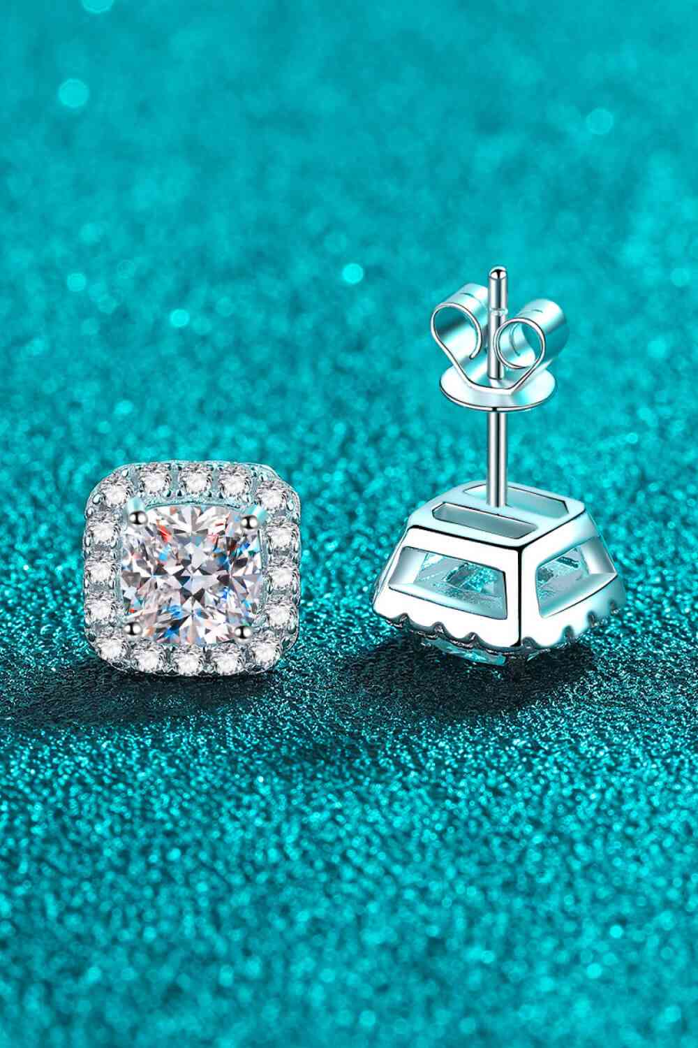 a pair of diamond stud earrings sitting on top of a blue surface