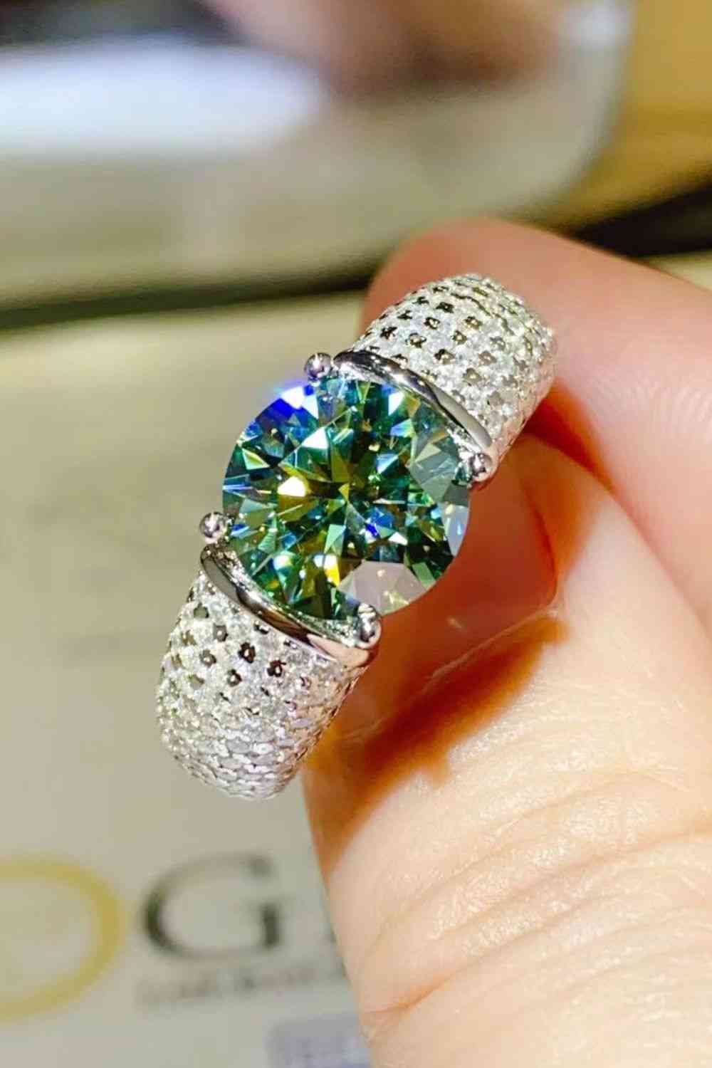 a woman's hand holding a ring with a green diamond