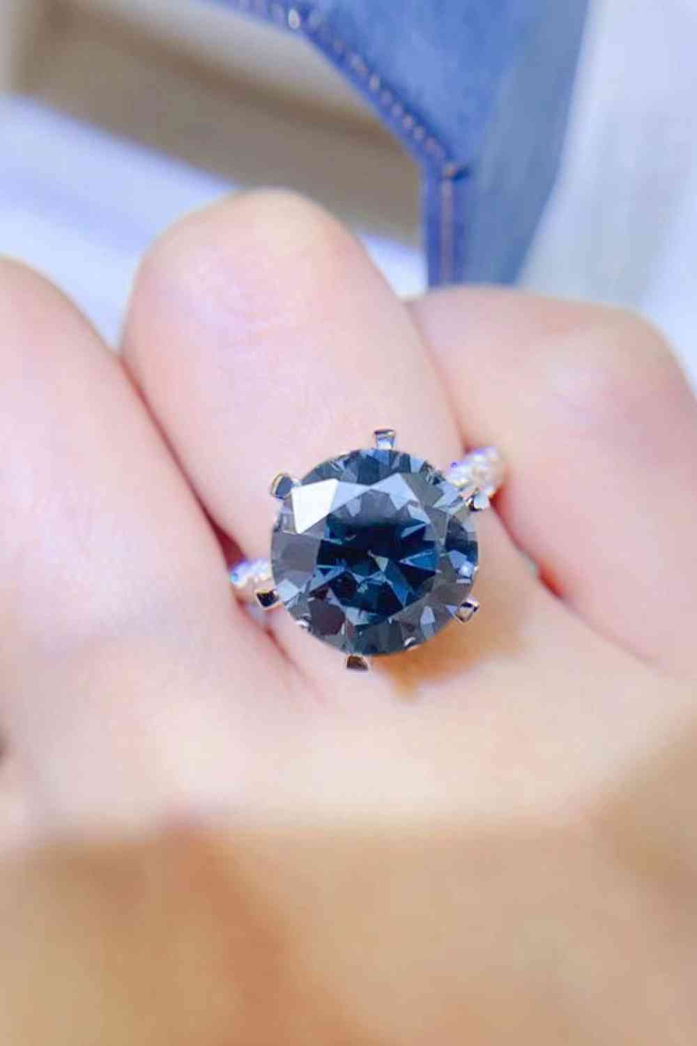 a close up of a person's hand holding a ring with a blue diamond