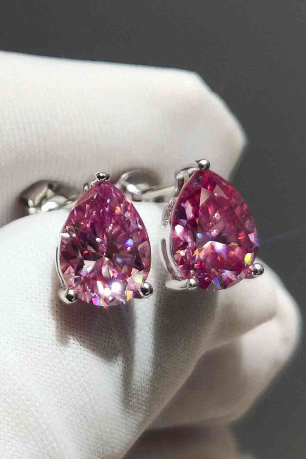 a pair of pink diamond earrings sitting on top of a white glove