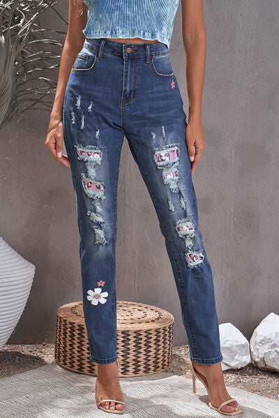 a woman standing in front of a plant wearing ripped jeans