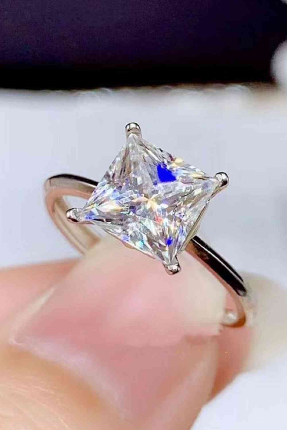 a close up of a person's hand holding a ring with a princess cut