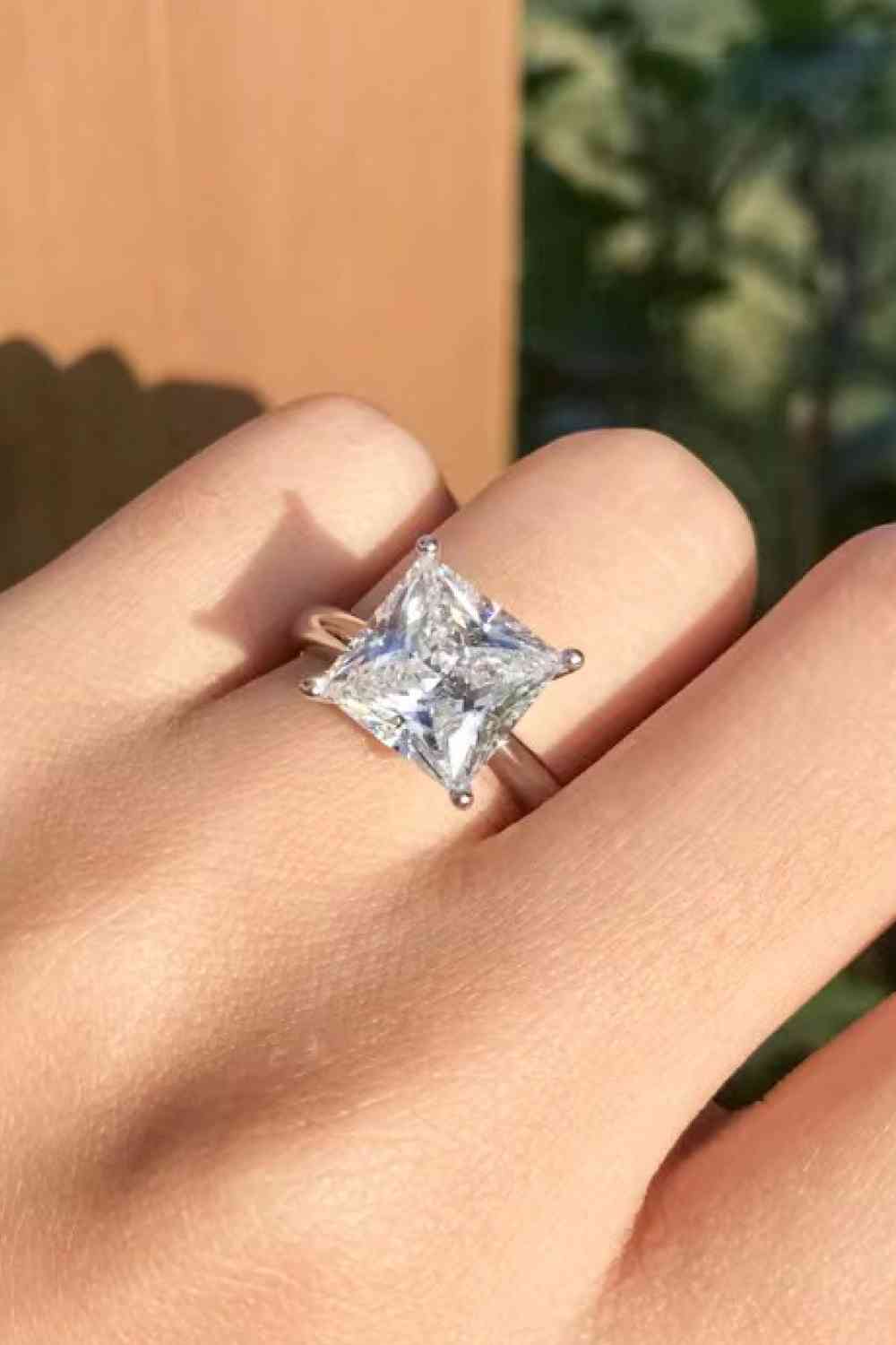 a close up of a person's hand wearing a ring with a princess cut
