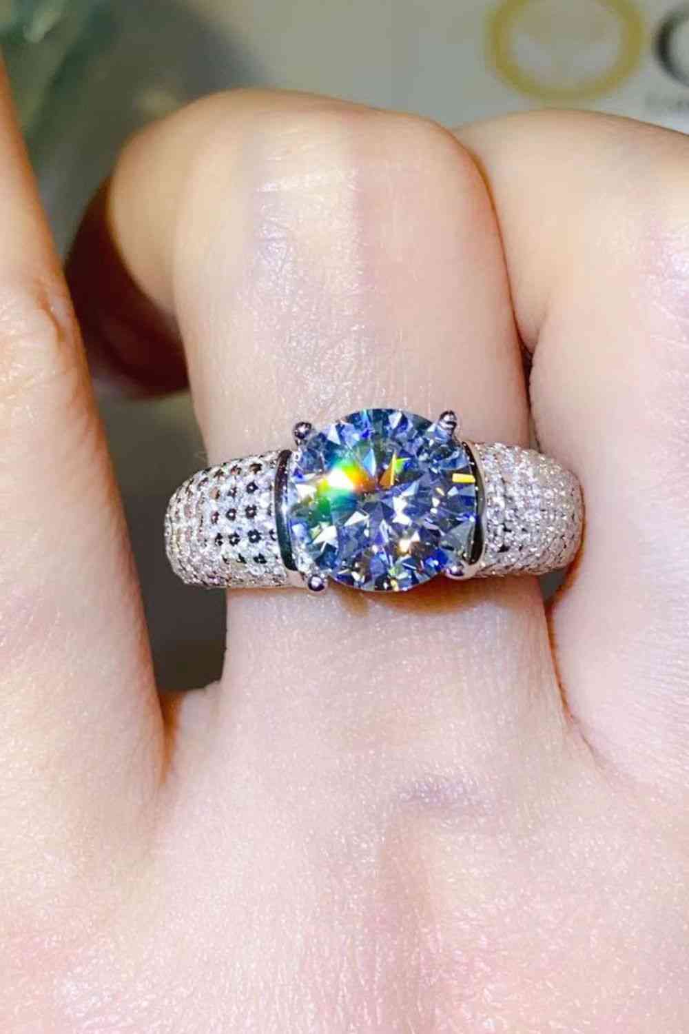 a woman's hand holding a ring with a rainbow colored diamond