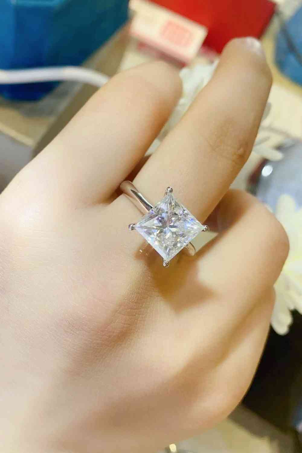 a woman's hand holding a ring with a princess cut diamond