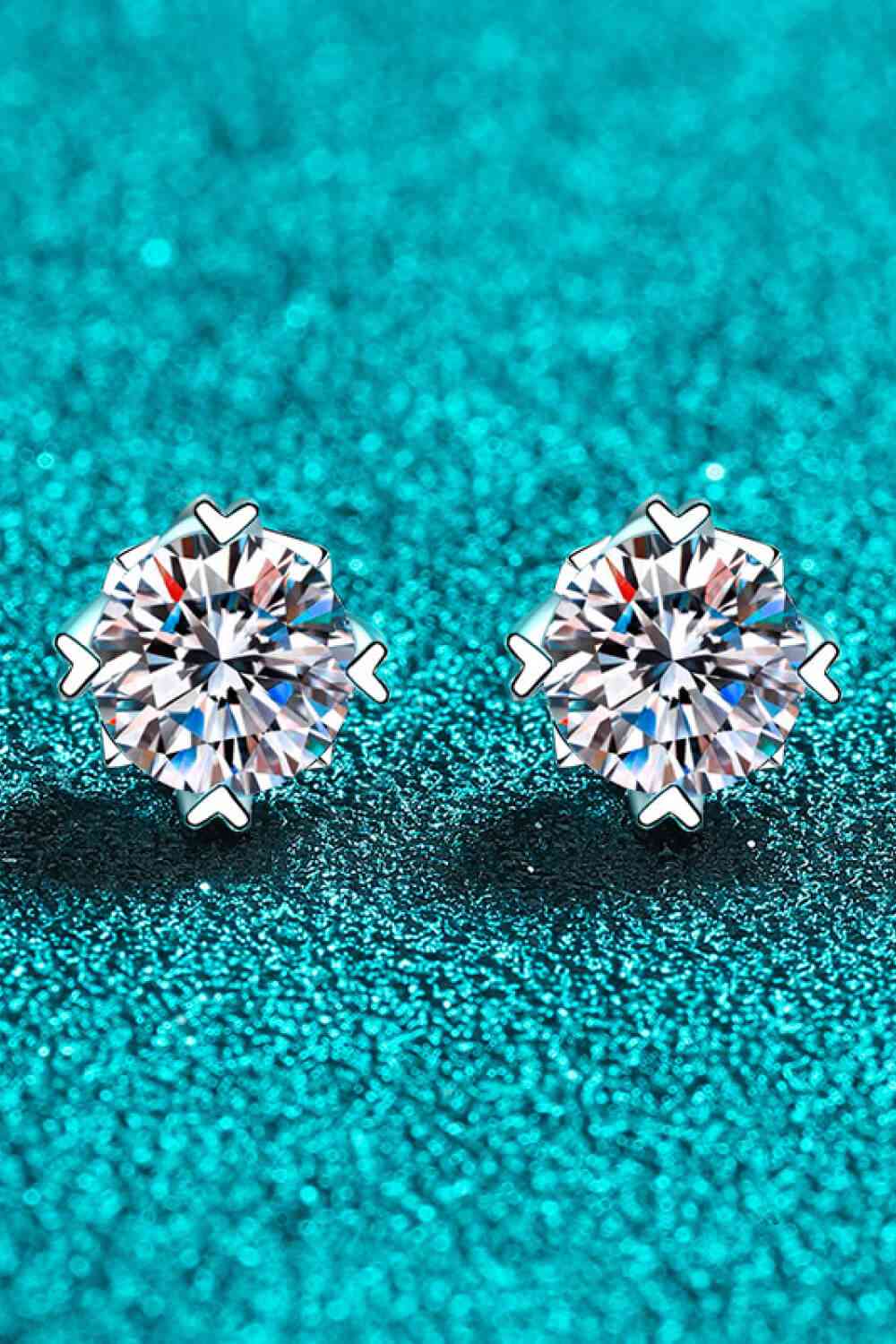 a pair of diamond earrings sitting on top of a blue surface