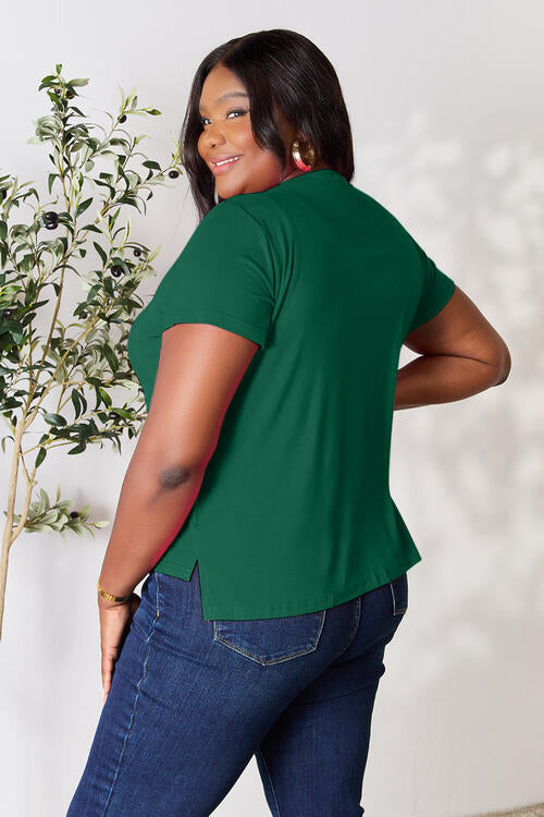 a woman wearing a green top and jeans pants standing next to a tree wearing a green shirt