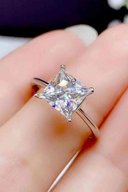 a close up of a person's hand holding a ring with a princess cut